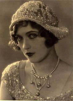 an old photo of a woman wearing a tiara and pearls on her head, looking at the camera