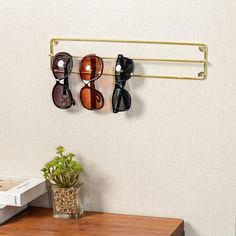 four pairs of sunglasses are hanging on a gold rack above a small potted plant