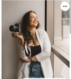 a woman holding a camera and smiling while standing next to a window with the caption that reads, what is your favorite photographer?