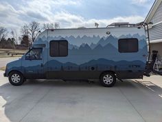 a camper parked in front of a house with mountains painted on it's side