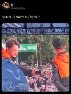 two men in orange vests shake hands at an event with a large crowd behind them