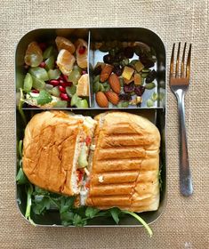 a sandwich and salad in a lunch box with a fork on the table next to it