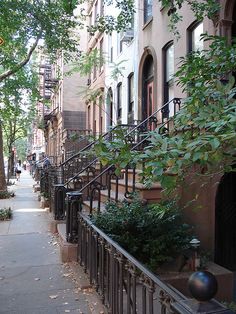 an alleyway in the city with many trees and buildings on both sides, lined with wrought iron railings