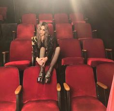 a woman is sitting in the middle of a row of red chairs with her legs crossed