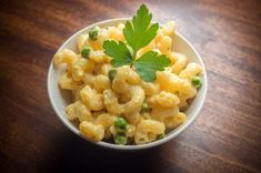 a white bowl filled with macaroni and peas on top of a wooden table