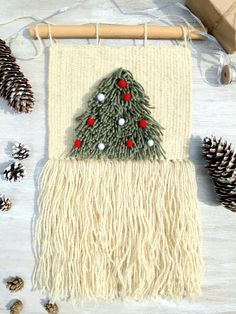 a small christmas tree is hanging on a wooden hanger next to pine cones and twine