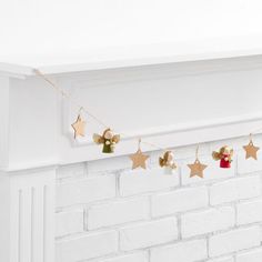 gold stars and bells are hanging from a string on a white brick fireplace mantel