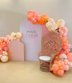 an orange and white balloon arch with peaches on the top, along with a pink chair