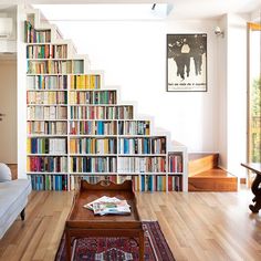 a living room filled with lots of books on top of a hard wood floor next to a stair case