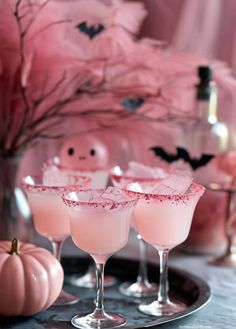 three glasses filled with pink liquid sitting on top of a metal tray next to halloween decorations