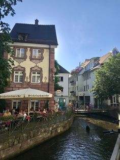 people are sitting at tables on the side of a river in an old european town