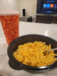 a bowl of macaroni and cheese next to a cup of soda on a table