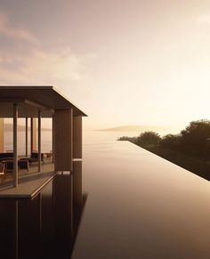 an empty swimming pool next to the ocean with chairs and tables on it at sunset