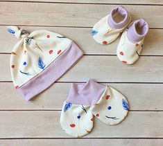 two pairs of baby booties and one hat are laid out on a wooden floor