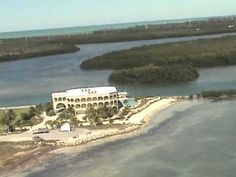 an aerial view of a building on the shore with water and land in the background