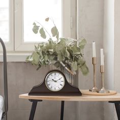 a clock sitting on top of a wooden table next to a vase filled with flowers