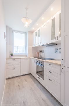 an empty kitchen with white cabinets and wood floors