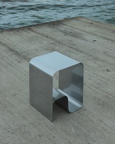 a square metal object sitting on top of a wooden pier next to the ocean with water in the background