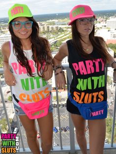 two young women standing next to each other on a balcony wearing party shirts and hats