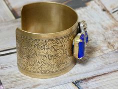 This bracelet is a brass metal cuff with a repurposed vintage repurposed brooch glued on top. A great gift for the vintage lover in your life. IT E M ∙ S P E C I F I C A T I O N S: - CUFF: Metal cuff is brass with a engraved floral detail and measures 6" X 1 1/2" - EMBELLISHMENT: Blue and clear rhinestone brooch is prong set and measures 1 1/2" x 1 1/8" C A R E ∙ T I P S: We don’t want your special moment to fade. To maintain the quality of your jewelry, please: - Do not wear it to the pool, spa Vintage Handmade Cuff Bracelet For Formal Occasions, Handmade Vintage Cuff Bracelet For Formal Occasions, Handmade Vintage Cuff Bracelet For Formal Events, Formal Vintage Handmade Cuff Bracelet, Costume Jewelry Cuff Bangle Bracelet For Gift, Vintage Brass Bracelet Gift, Vintage Antique Gold Cuff Bangle Bracelet, Vintage Antique Gold Cuff Bangle, Vintage Antique Gold Bangle Cuff Bracelet