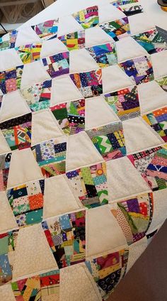 a quilted table top with many different colored squares on it and a vase in the background