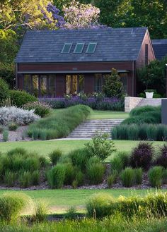 the house is surrounded by lush green grass and shrubs, with purple flowers in the foreground