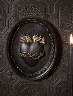 two candles are lit next to a black wall with a heart shaped decoration on it