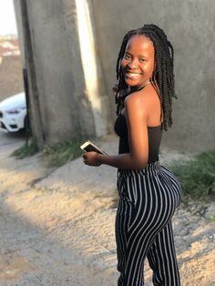 a woman with dreadlocks is smiling and holding a book in her hand while walking down the street