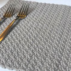 two forks are sitting on top of a crocheted placemat that is made out of yarn