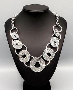 "Industrial Envy": Gradually increasing in size near the center, a collection of shiny silver rings and abstract hammered discs interlock below the collar for an intense industrial look. Features an adjustable clasp closure. Sold as one individual necklace. Includes one pair of matching earrings. Modern Circular Metal Jewelry, Modern Hammered Metal Necklace, Hammered Metal Circle Jewelry, Modern Metallic Metal Jewelry, Hammered Silver Jewelry For Party, Unique Metallic Metal Jewelry, Metallic Metal Chain Jewelry, Nickel-free Metallic Metal Jewelry, Adjustable Hammered Metal Necklaces