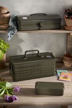 two green suitcases sitting on top of a wooden table next to potted plants