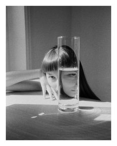 a woman laying down behind a glass with water in it