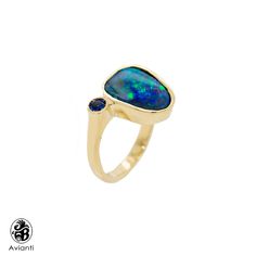 "Surprise her with this stunning blue boulder opal ring. The center stone is an squarish Pear cut natural boulder Australian Opal and is cast in 14 Karat yellow gold, with shiny finish with an accent of bezel set Sapphire stone. This ring is from our \"Opalescence \" collection. Each stone is unique in cut and color. This beautiful stone displays a green and blue hue that compliment each other in every way. [MATERIALS] Stone: Opal (1) Cut: Pear Carat: 3.03 Play of color: blue green hues Transpar Unique Opal Ring, Yellow Gold Opal Ring, Gold Opal Ring, Flower Diamond Ring, Boulder Opal Ring, Purple Opal, Unique Opal, Opal Ring Gold, Green Hues