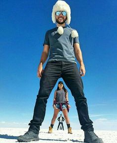 a man standing on top of a snow covered slope next to a woman wearing skis