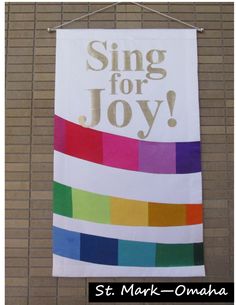 a banner hanging on the side of a building that says sing for joy with rainbow colors