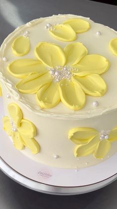 a white cake with yellow flowers and pearls on the top is sitting on a plate