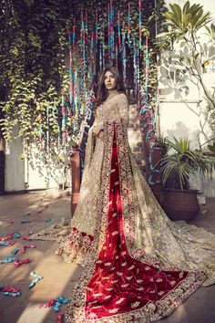 a woman in a red and gold bridal gown standing on the ground with flowers around her