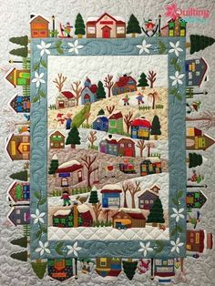 a quilted wall hanging with houses and trees in the snow on top of it