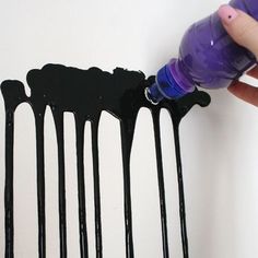 a hand is holding a purple bottle and dripping black paint on a white wall