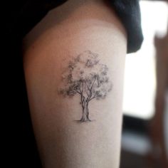 a woman's arm with a small tree tattoo on the back of her shoulder