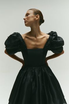 a woman wearing a black dress with puffy sleeves and an open back, standing in front of a white background