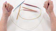 two hands are holding knitting needles on a white surface