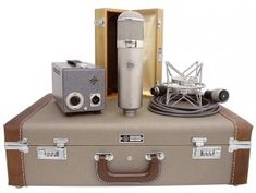 an old suitcase with two microphones and a radio on top, sitting next to it