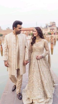 a man and woman standing next to each other in front of the water holding hands