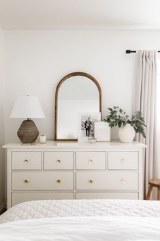 a bedroom with white furniture and a large mirror on top of the dresser next to it