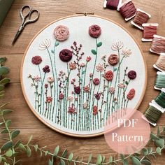 a close up of a embroidery on a wooden table with scissors and flowers in the hoop