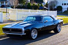 a black muscle car parked in front of a white picket fence