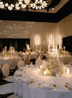 a room filled with lots of tables covered in white linens and gold place settings