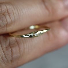 a woman's hand holding a gold ring with two small diamonds on the side