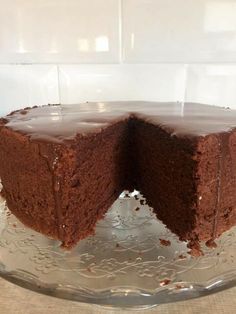 a chocolate cake with one slice taken out of it on a glass platter in front of a white tile wall